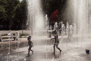 Kids running through water spray fountains in a park.