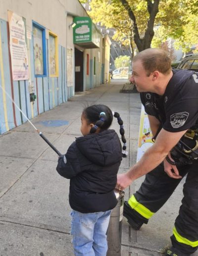 NYC firefighter helps a child use a fire extinguisher during a visit to Luminous.