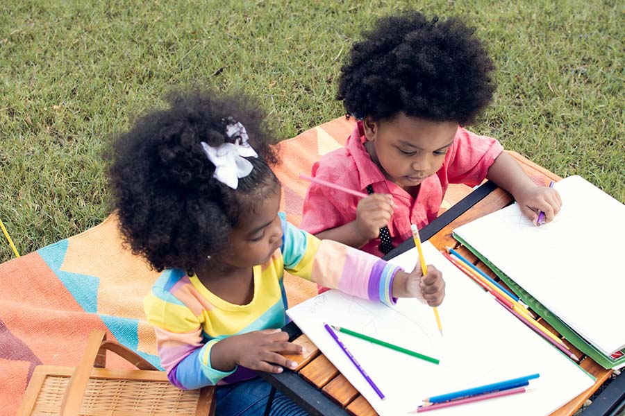 Two children draw on paper outside.