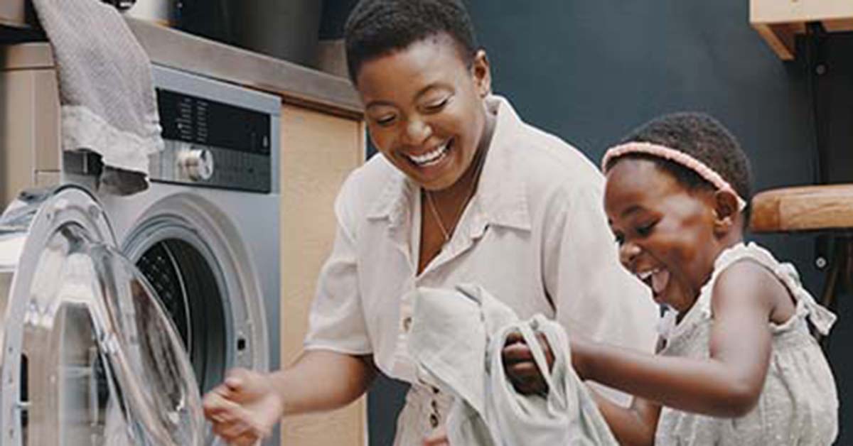 Happy mom and daughter folding clothes from a dryer.