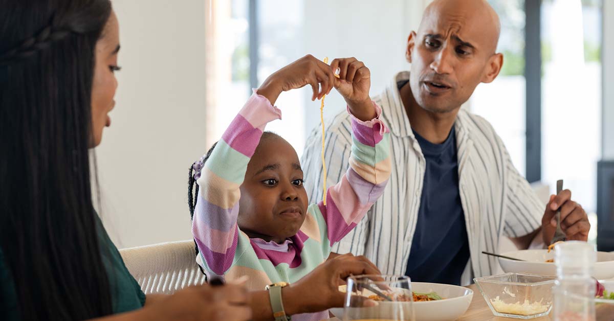 Diverse family sharing spaghetti meal in home dining room with white bowls and orange juice