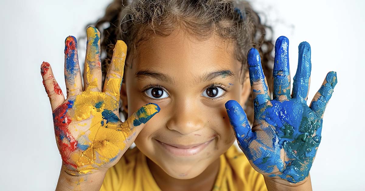 A young girl holds up the palms of her hands covered in paint.