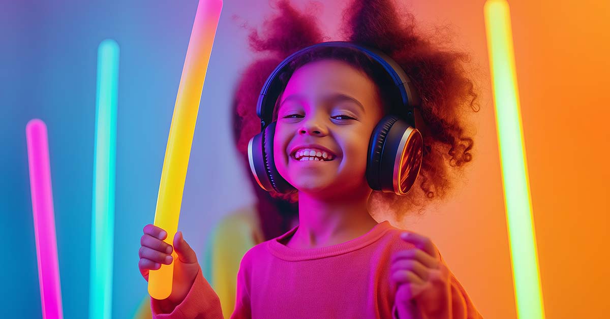 Smiling toddler girl wearing head phones dances among glowing light sticks.
