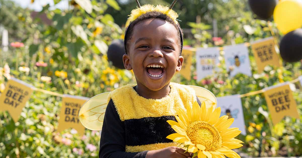 Laughing toddler boy wearing a bee costume and holding a large yellow sunflower.