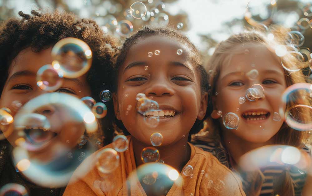 3 smiling young children playing with bubbles.