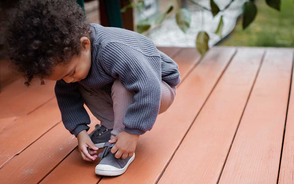 Toddler adjusts straps on his shoes as he prepares for preschool.