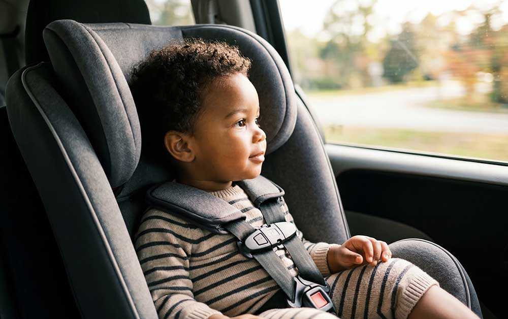 Toddler boy in a car seat looking out a car window.