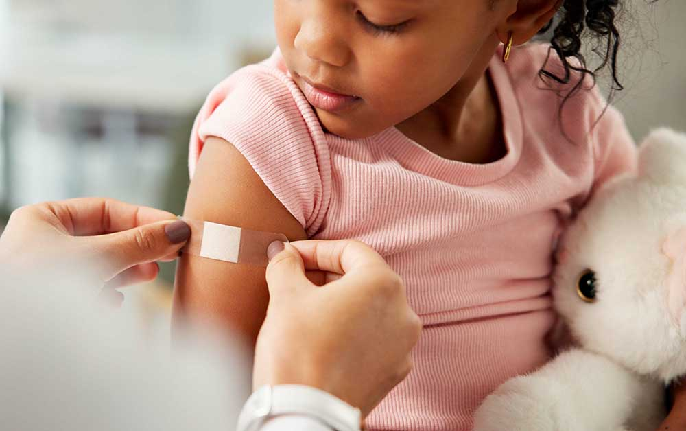 Health care worker places a band-aid on a oddler girl.